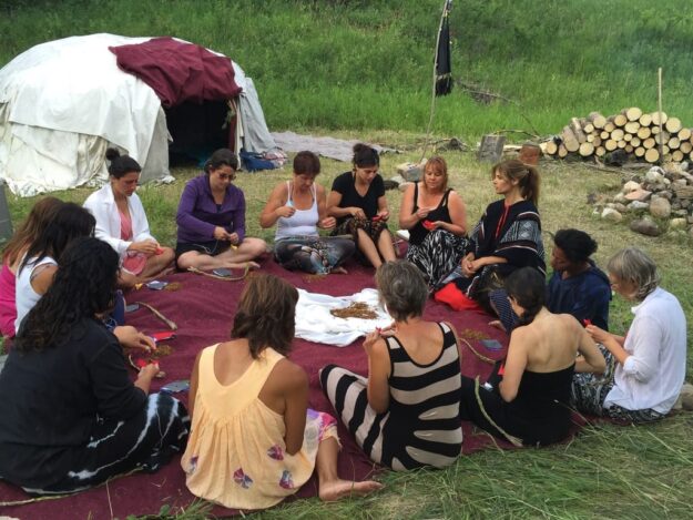 A group of people sitting on the ground in front of a tent.