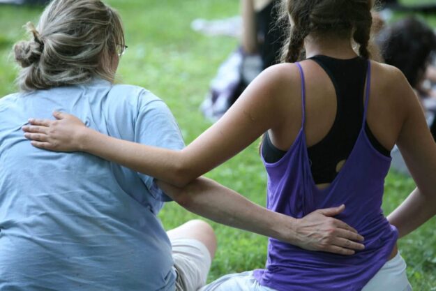 Two women are holding hands while sitting on the grass.