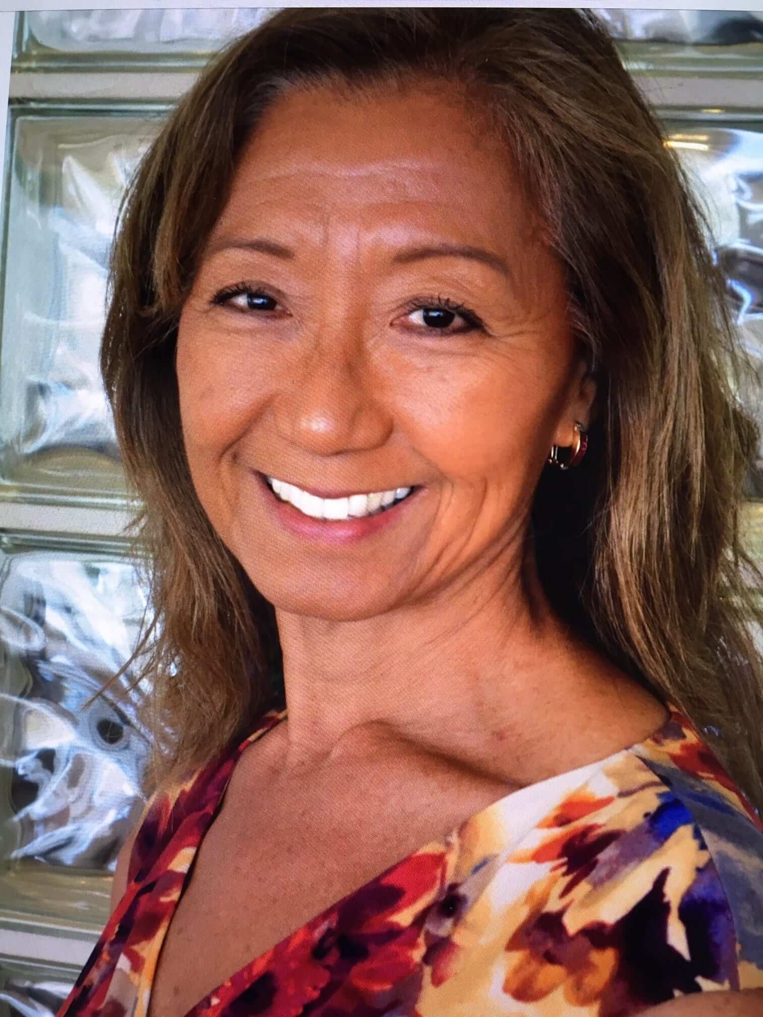 A woman with long hair and white teeth smiling.