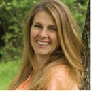A woman standing next to a tree smiling for the camera.