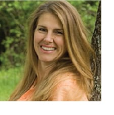 A woman standing next to a tree smiling for the camera.