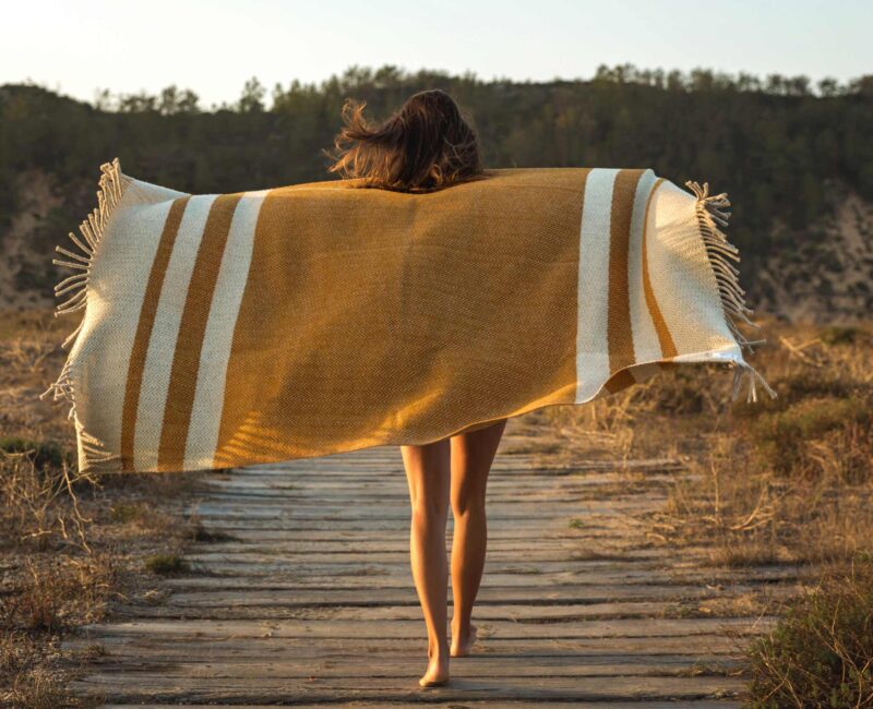 A woman walking on the boardwalk with her towel over her head.
