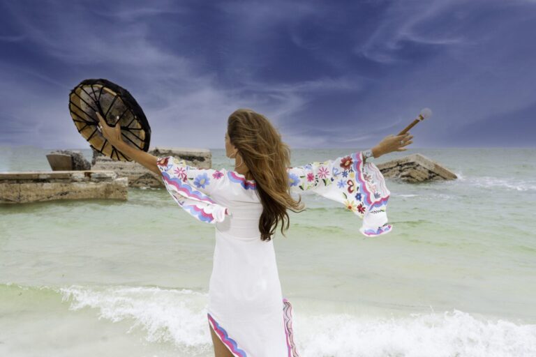 A woman in white dress holding an object on the beach.
