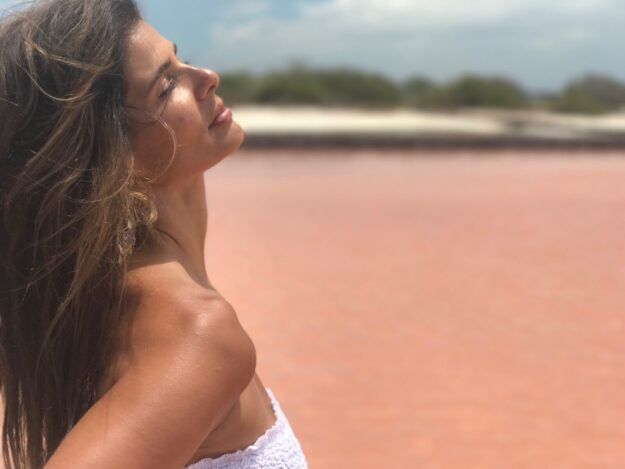 A woman in white shirt standing on beach near body of water.