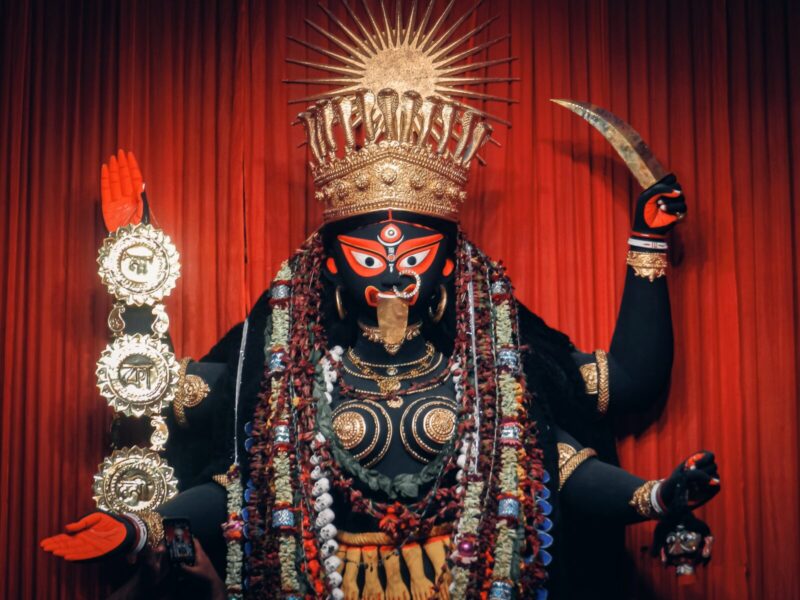 A statue of an indian deity with red curtains in the background.