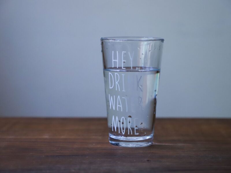 A glass of water with the words " hey, drink water more ".