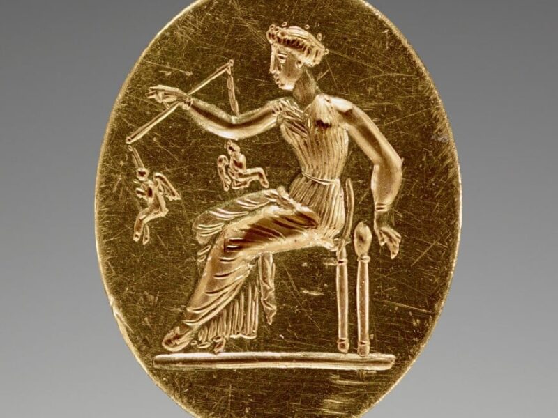 A gold medal with an image of a man sitting on a chair.
