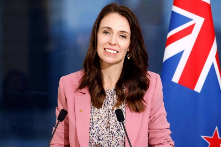 A woman in pink jacket standing at podium with flags.