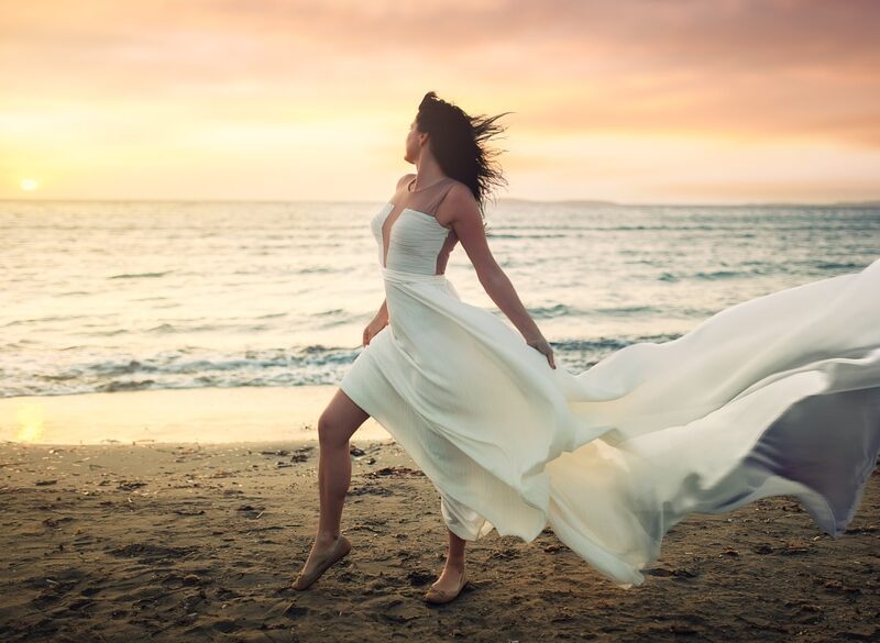 A woman in white dress on beach near water.