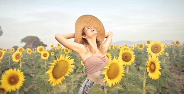 A woman in a hat is standing in the middle of sunflowers.