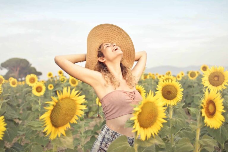 A woman in a hat is standing in the middle of sunflowers.