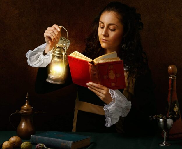 A woman is reading a book and holding a lamp.