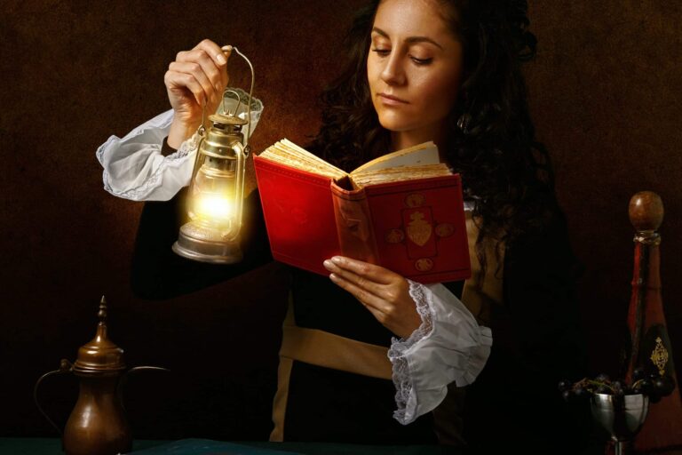 A woman is reading a book and holding a lamp.