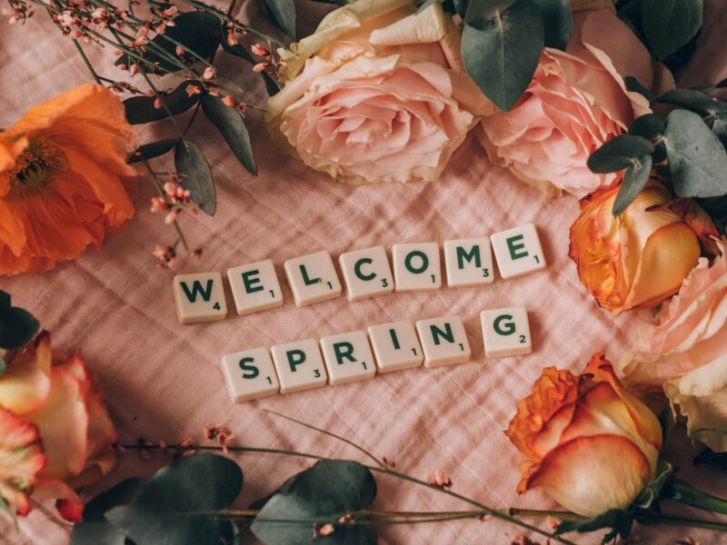 A pink blanket with flowers and scrabble tiles that say " welcome spring ".