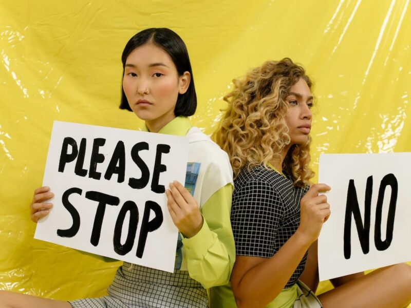 Two women holding signs that say please stop and no.