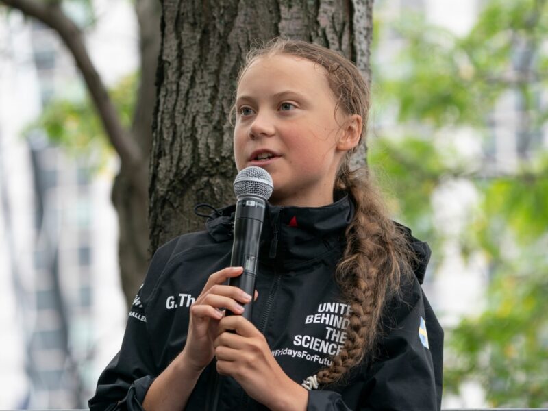 A young girl holding a microphone in front of a tree.