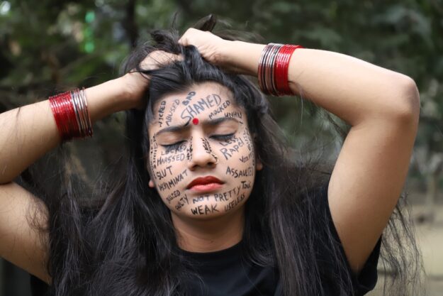 A woman with writing on her face and hands holding her hair.