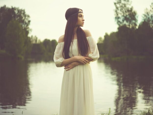 A woman in white dress standing next to water.