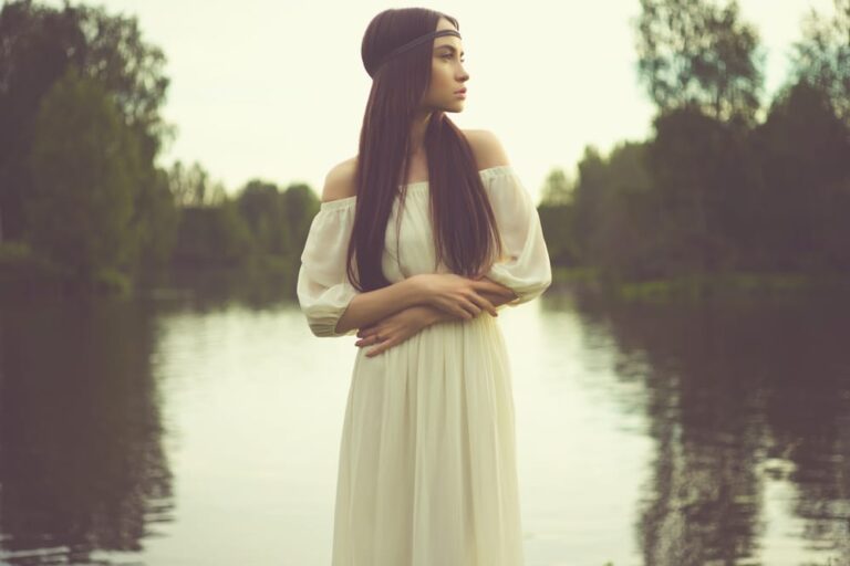 A woman in white dress standing next to water.