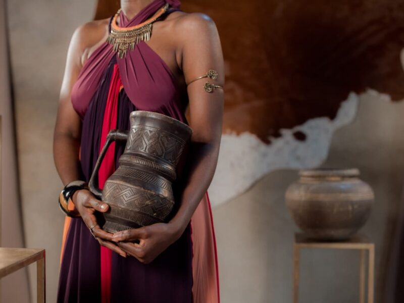 A woman in purple dress holding an old metal pot.