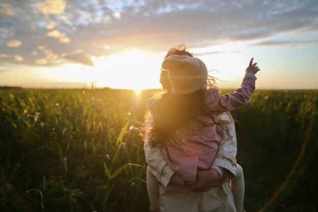 A woman in a field with the sun setting.