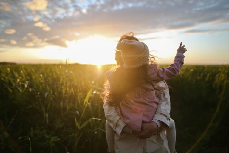 A woman in a field with the sun setting.