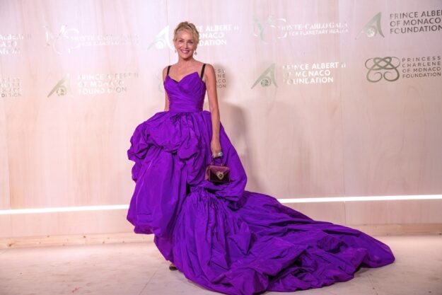 A woman in a purple dress standing next to a wall.