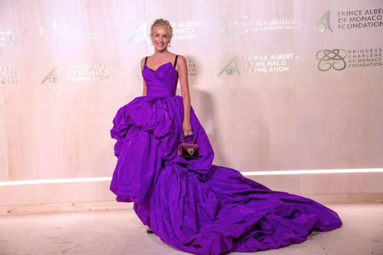 A woman in a purple dress standing next to a wall.