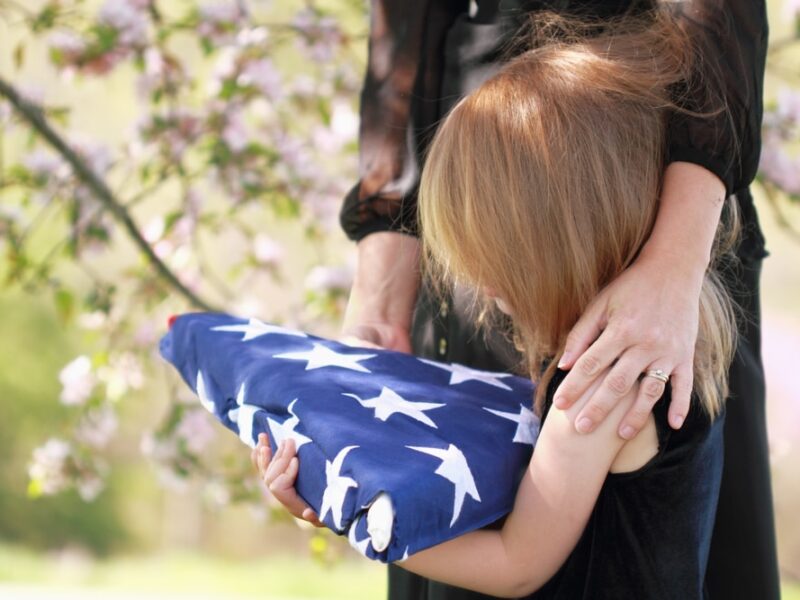 A woman holding an american flag with her arm around a child.